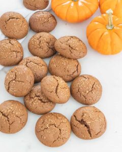 Several pumpkin molasses cookies sprinkled with sugar on white background with mini pumpkins.