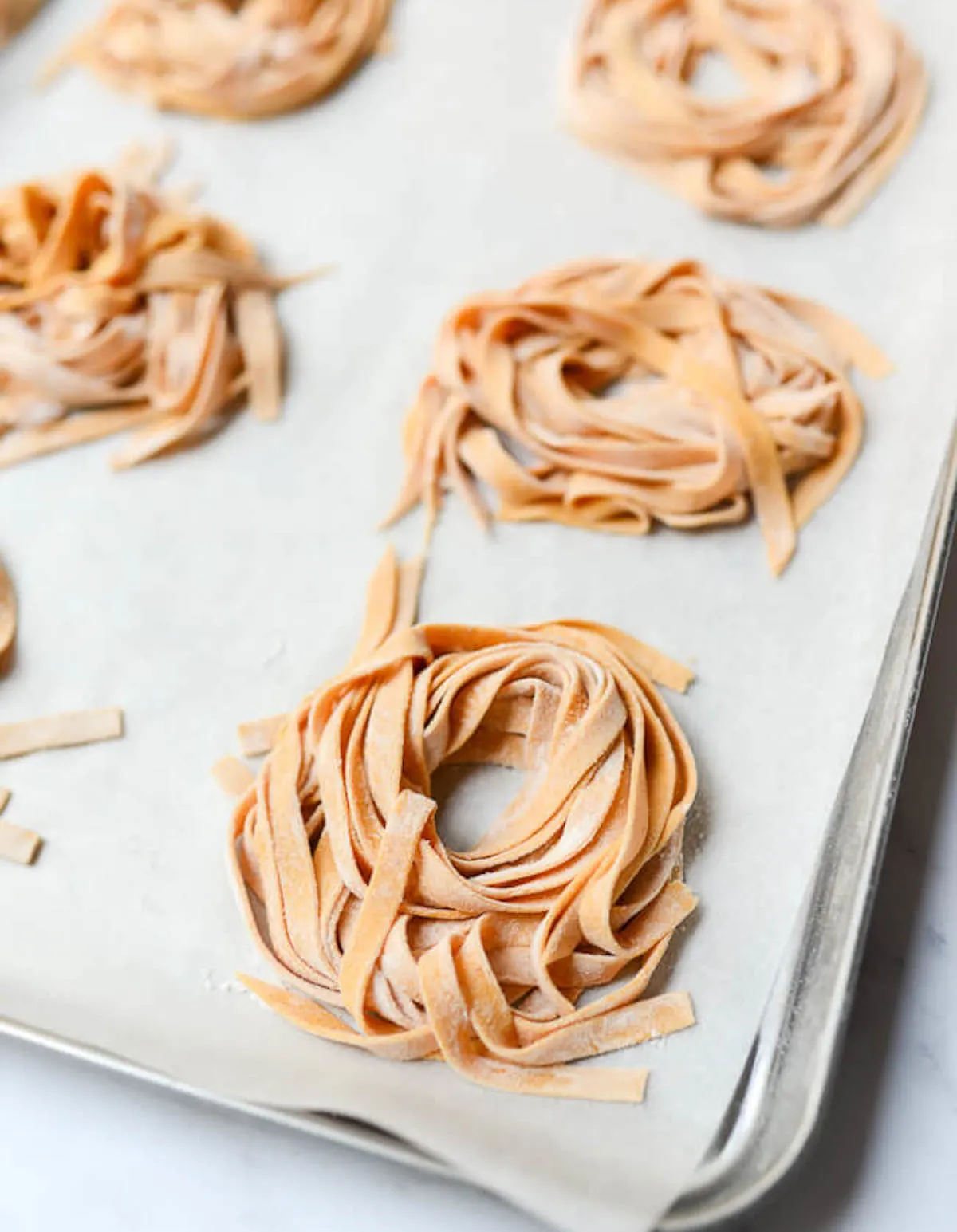 Pumpkin pasta fettuccine arranged in small piles over parchment paper on metal baking sheet.