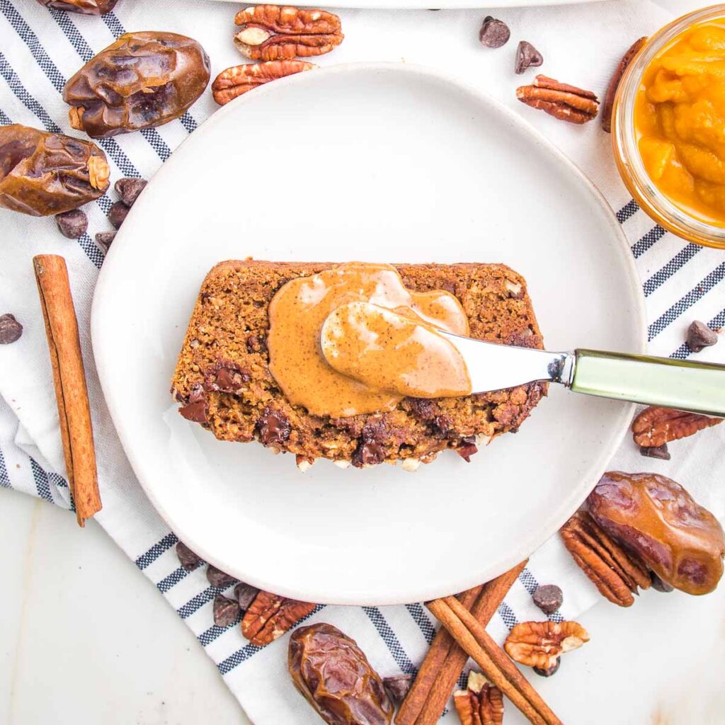 Piece of vegan pumpkin bread on white plate surrounded by whole dates and cinnamon sticks.