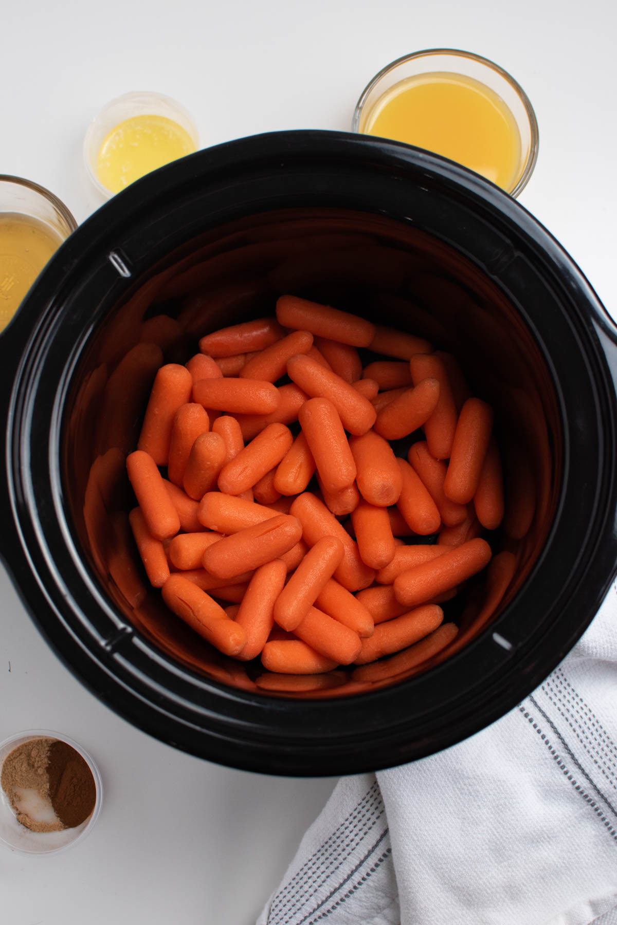 Several baby carrots in black Crockpot insert surrounded by other ingredients.