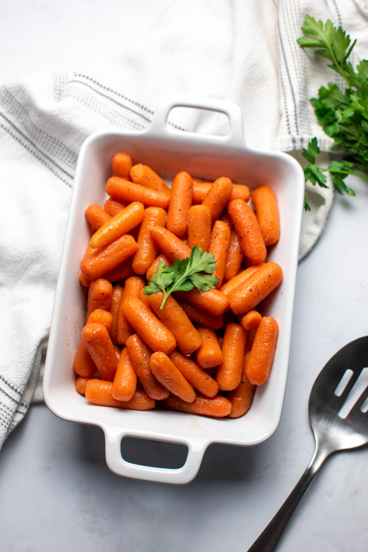 Small white baking dish full of brown sugar carrots with fresh parsley on top.