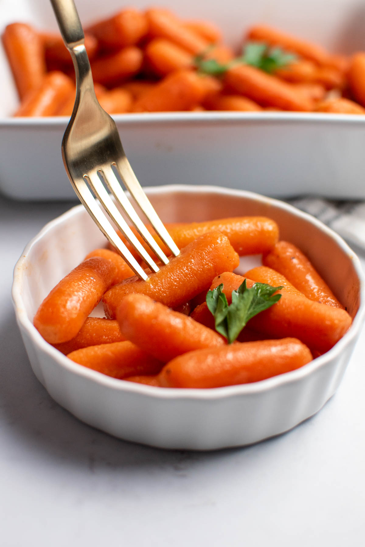 Gold fork pierces single carrot from ramekin full of brown sugar honey glazed carrots.