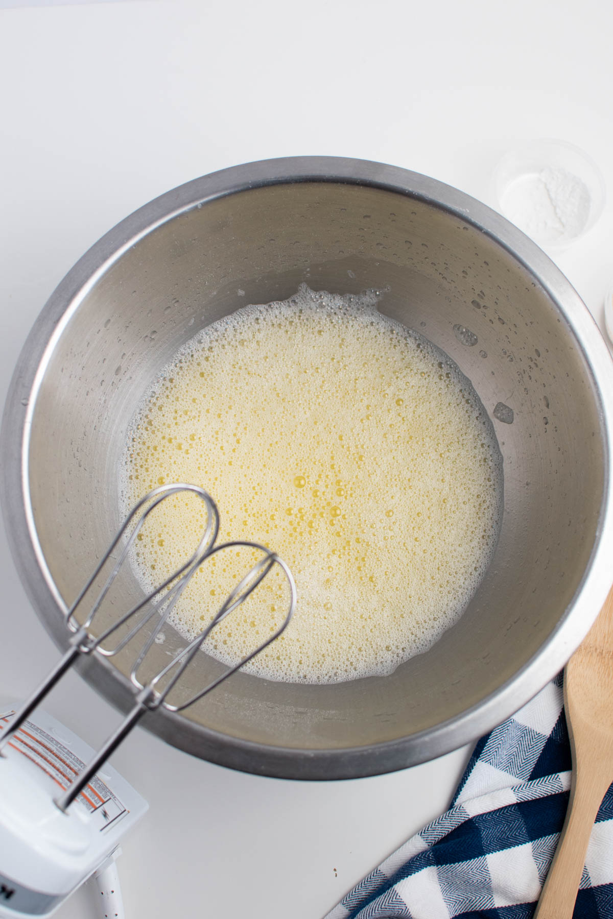 Butter, egg, and water mixture in large mixing bowl with electric beaters above bowl.
