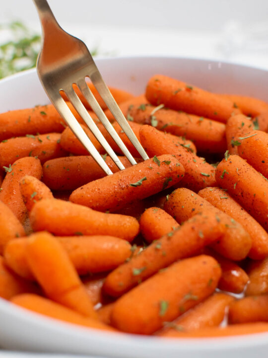 Gold fork pokes one cinnamon honey carrot in a bowlful of carrots.