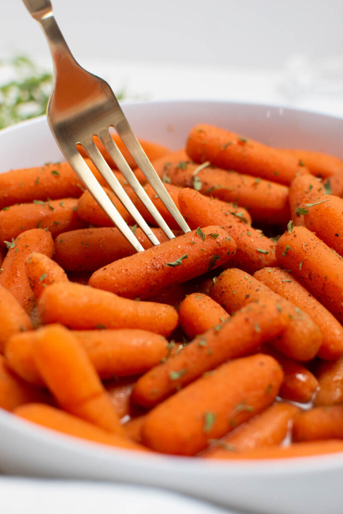 Gold fork pokes one cinnamon honey carrot in a bowlful of carrots.