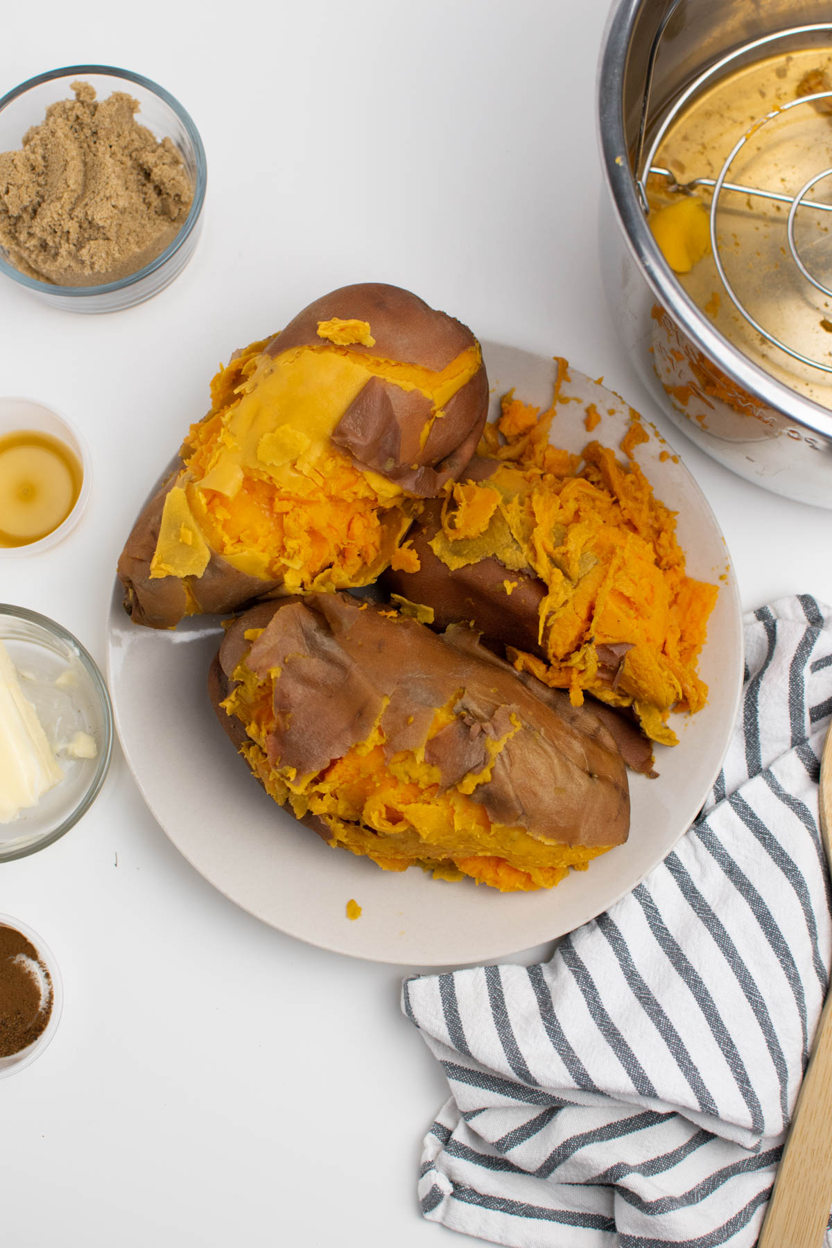 Cooked sweet potatoes with skins coming off on plate surrounded by various ingredients.