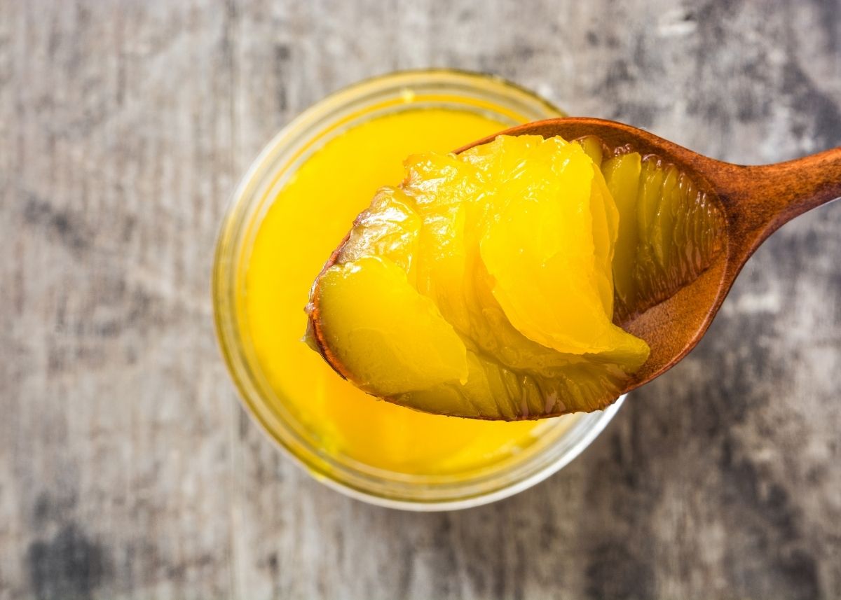 Large wooden spoon lifts dollop of bright yellow ghee from glass jar.