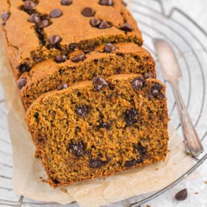 Sliced gluten free pumpkin bread with melting chocolate chips on brown parchment paper with knife.