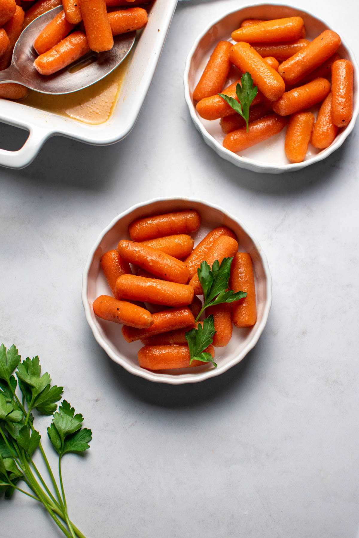 Two small ramekins with honey glazed carrots and fresh parsley on marble countertop.