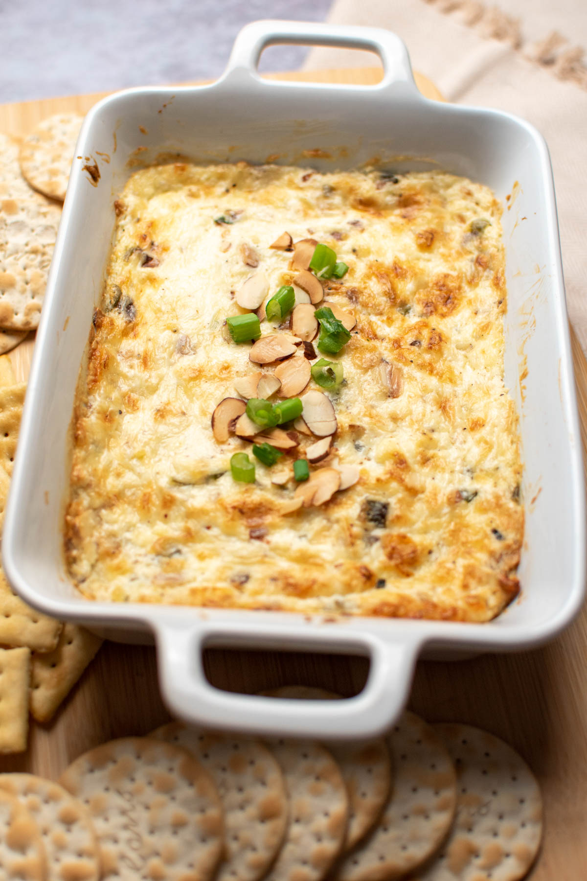 Small white baking dish with hot Swiss almond dip garnished with toasted almonds and green onion.