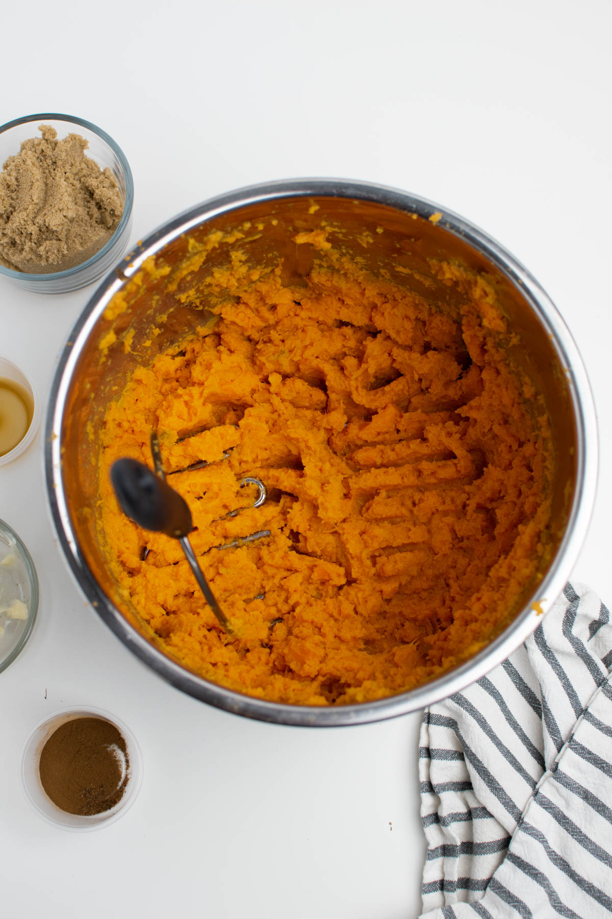 Mashed sweet potatoes in metal bowl with various ingredients also on table.