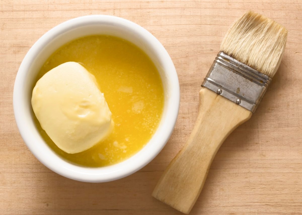 Melted butter in small white mixing bowl next to wooden basting brush.