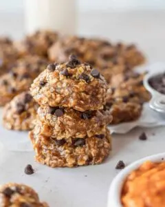 Close up of stack of no bake pumpkin cookies with chocolate chips next to bowl of pumpkin puree.