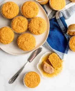 Several pumpkin cornbread muffins on a white plate next to blue and white kitchen towel.