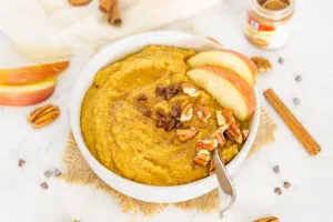 Pumpkin cream of wheat in large white bowl with mini chocolate chips, apple and pecans.