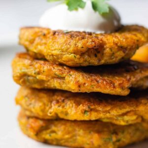 Stack of 4 pumpkin fritters topped with sour cream and parsley leaves.