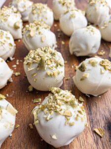 Close up of several pumpkin gingersnap cookie pops with white coating and chopped pistachios on top.