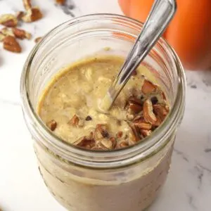 Close up of jar of pumpkin pie overnight oats with pecans on top with spoon.