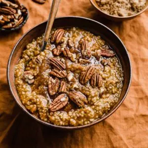 Brown bowl full of pumpkin steel cut oats and pecans on orange tablecloth.