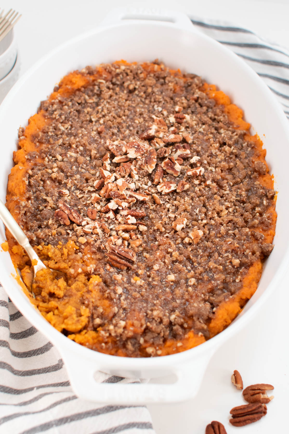 Sweet potato crunch casserole in white baking dish with gold spoon resting inside of casserole.