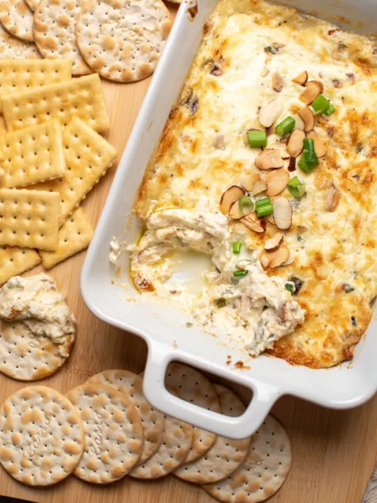 White baking dish with empty space and Swiss cheese dip next to assorted crackers.