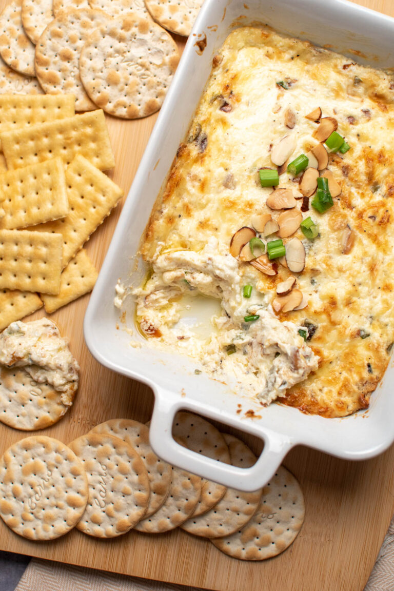 White baking dish with empty space and Swiss cheese dip next to assorted crackers.