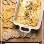 Pinterest graphic with text and photo of toasted almond swiss cheese dip in white baking dish.