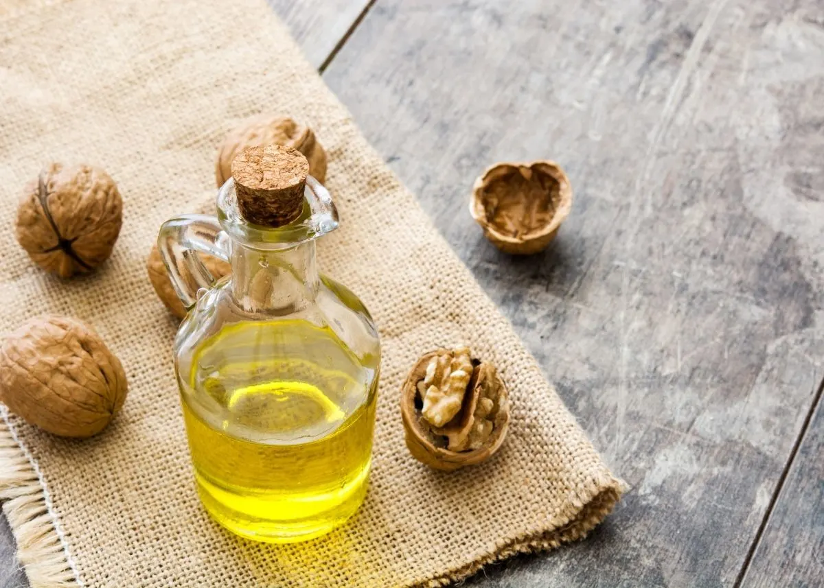 Large glass bottle of walnut oil on burlap cloth surrounded by walnuts.