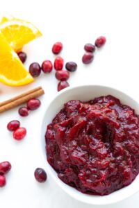 Bowl of cranberry orange sauce with scattered cranberries and orange slices.