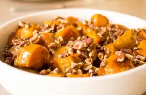 Close up of glazed sweet potatoes with pecans in large white serving bowl.