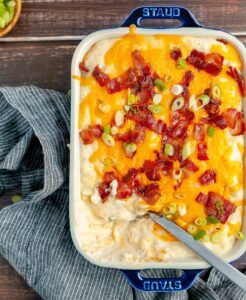 Loaded mashed potatoes with bacon and green onion on top with blue kitchen towel.