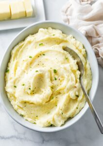 Large bowl of mashed potatoes with green garnish for Christmas dinner.