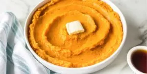 Mashed sweet potato with cube of butter in center in white bowl.