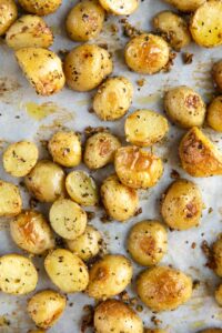 Sheet pan of roasted potato pieces flecked with seasonings on parchment paper.