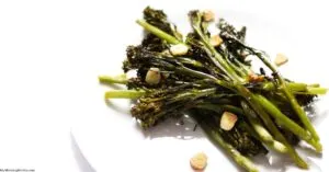 Close up of roasted tenderstem broccoli with garlic slices on white plate.