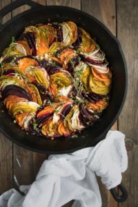 Skillet of scalloped root vegetables with white towel nearby.