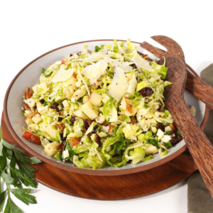 Shaved brussels sprouts salad with apples and pecans and wooden spoons.
