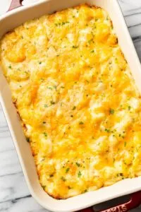 Cheesy potatoes casserole in large rectangular baking dish with sprinkled green garnish.