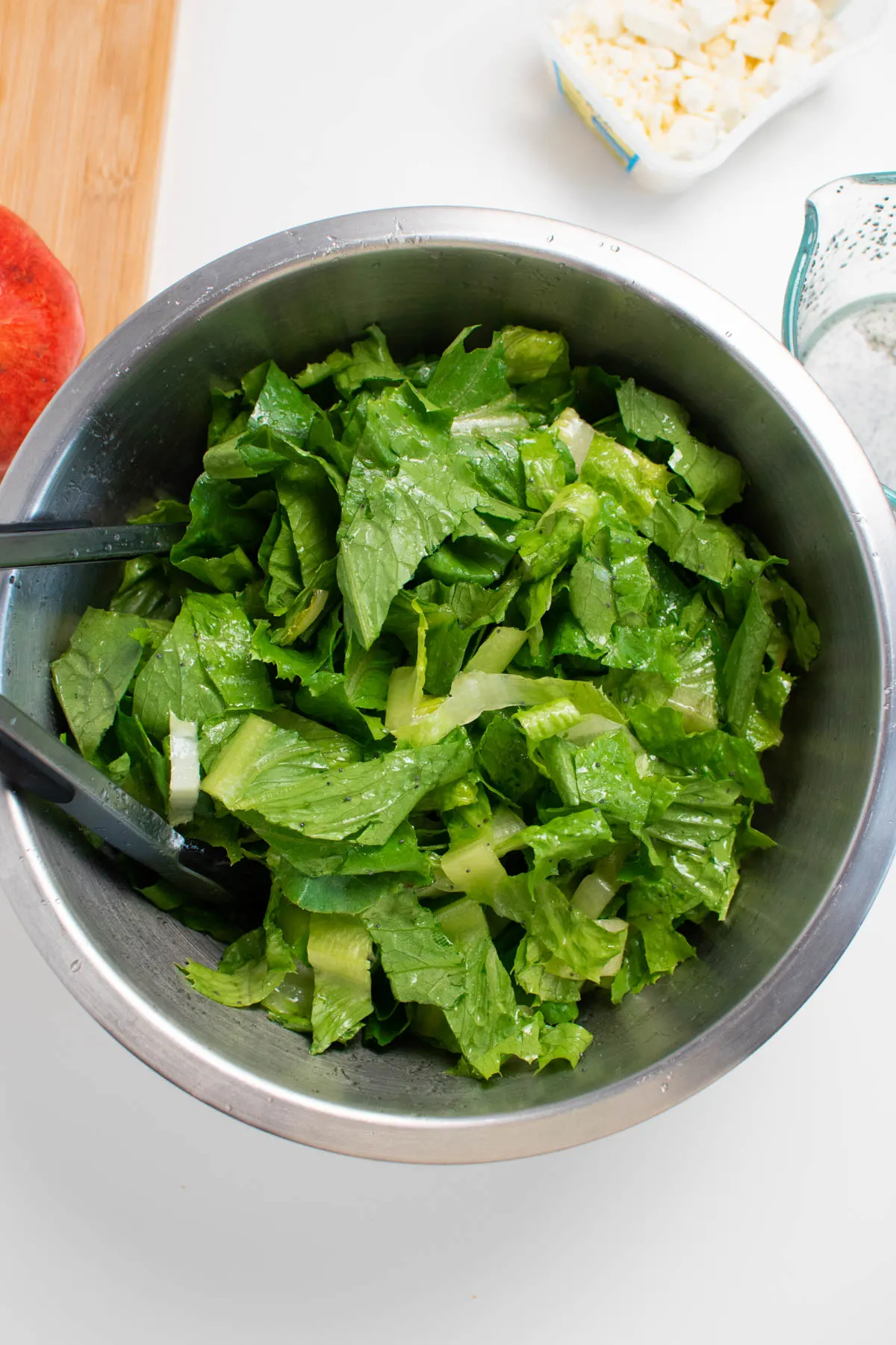 Chopped lettuce coated in poppy seed dressing in large salad bowl with tongs.