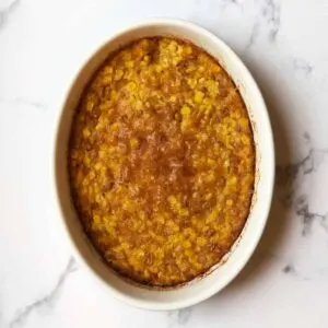 Baked corn soufflé in large white casserole baking dish on marble counter.