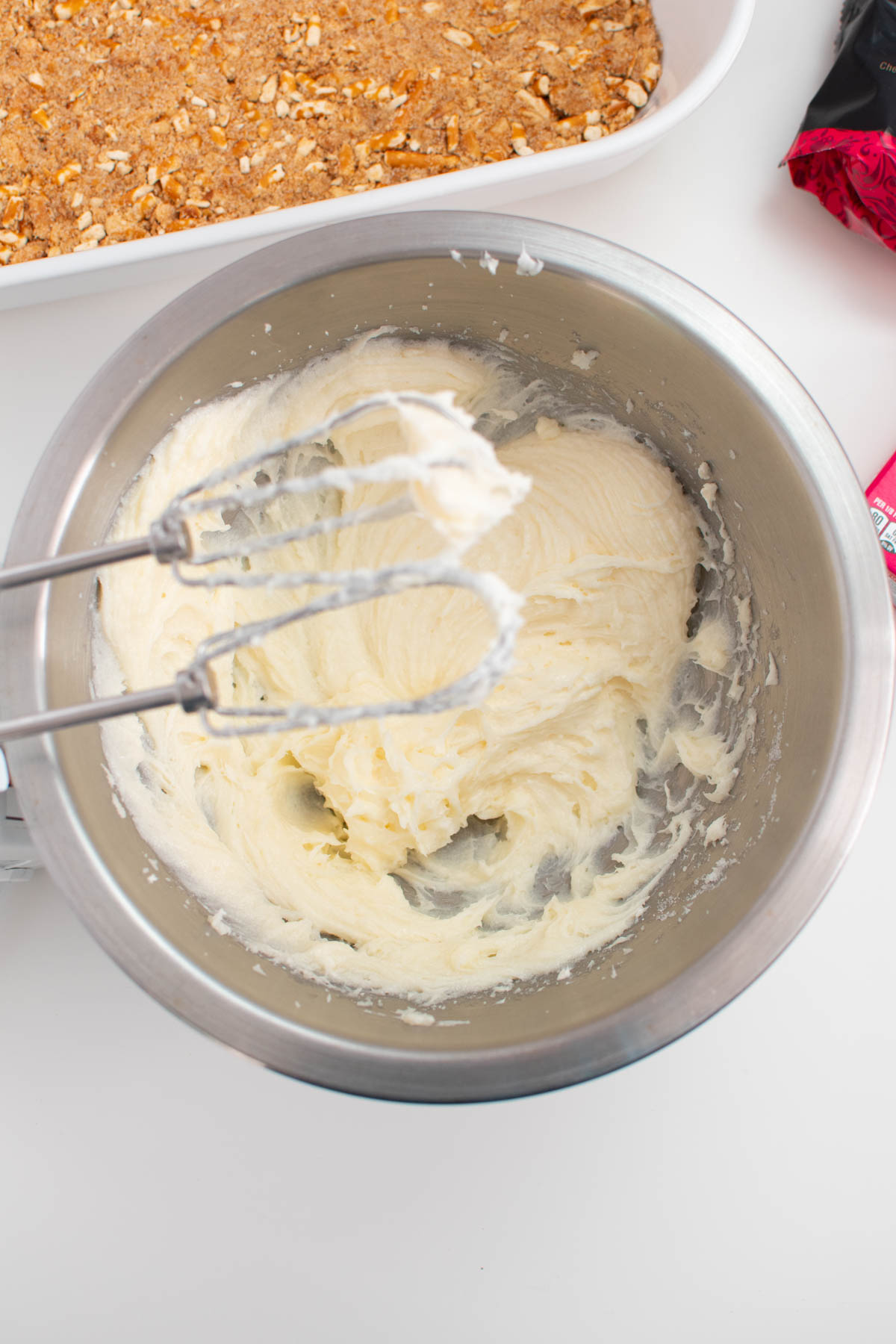 Whipped cream cheese mixture in metal mixing bowl with beaters above.