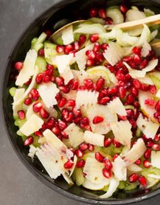 Celery salad with pomegranate arils and cheese in black serving dish with gold spoon.