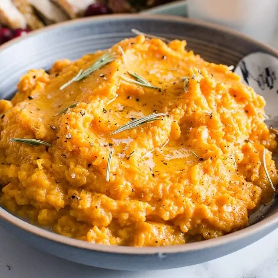 Blue bowl with mashed sweet potatoes and rosemary sprigs.