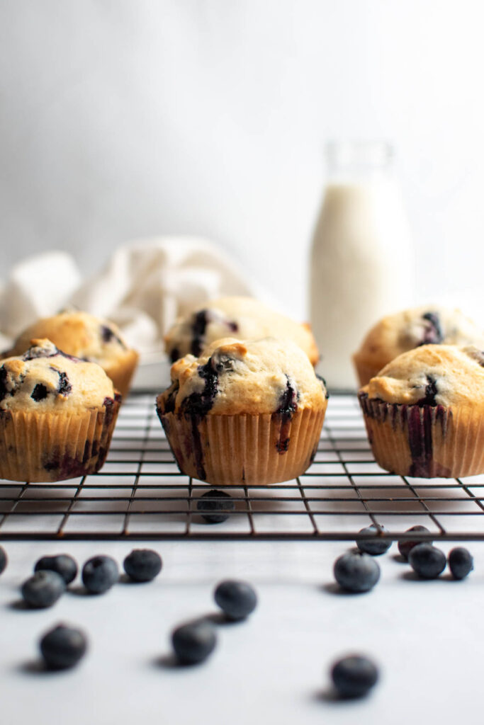 Fluffy blueberry muffins on baking rack with fresh blueberries scattered on counter.