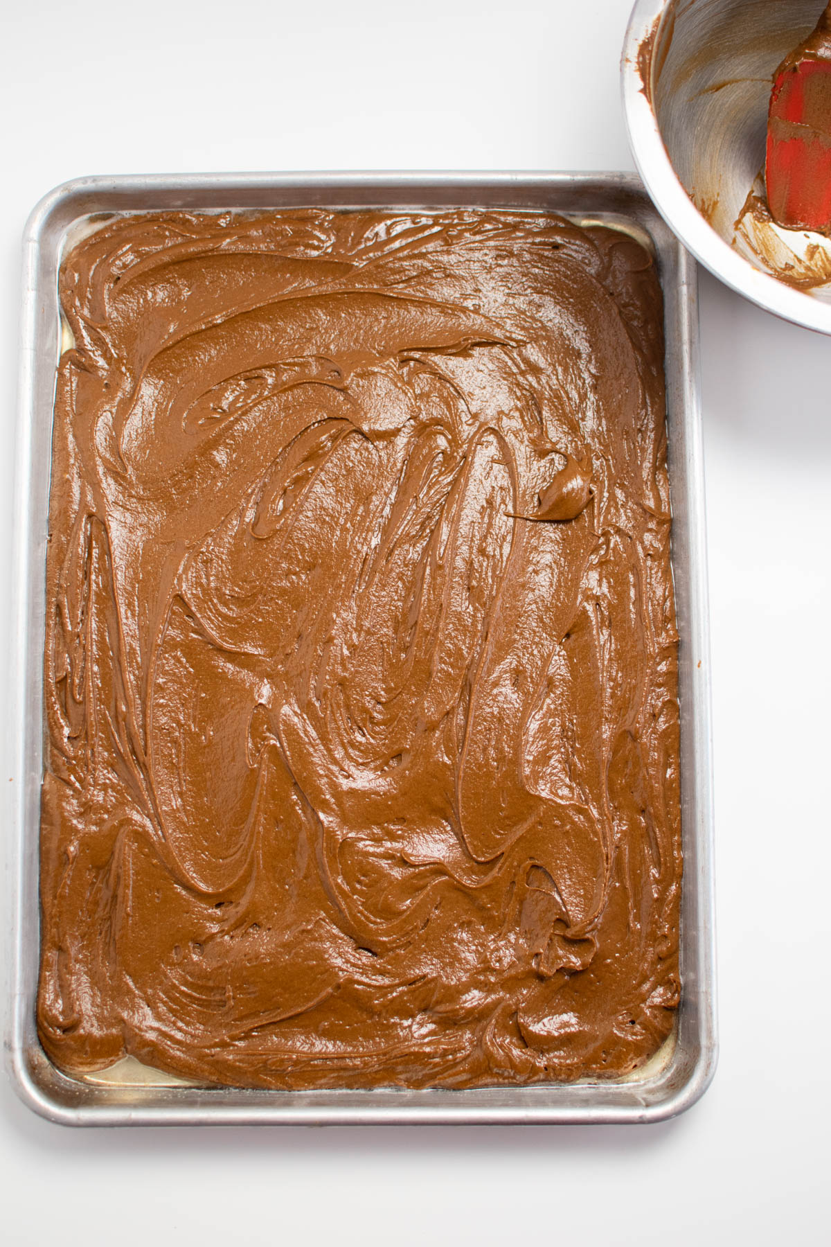 Gingerbread batter in metal sheet pan with empty bowl nearby.