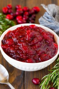 Homemade cranberry sauce in decorate white serving dish and scattered fresh cranberries.