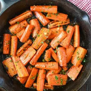 Lightly charred honey garlic roasted carrots with green garnish in large black skillet.