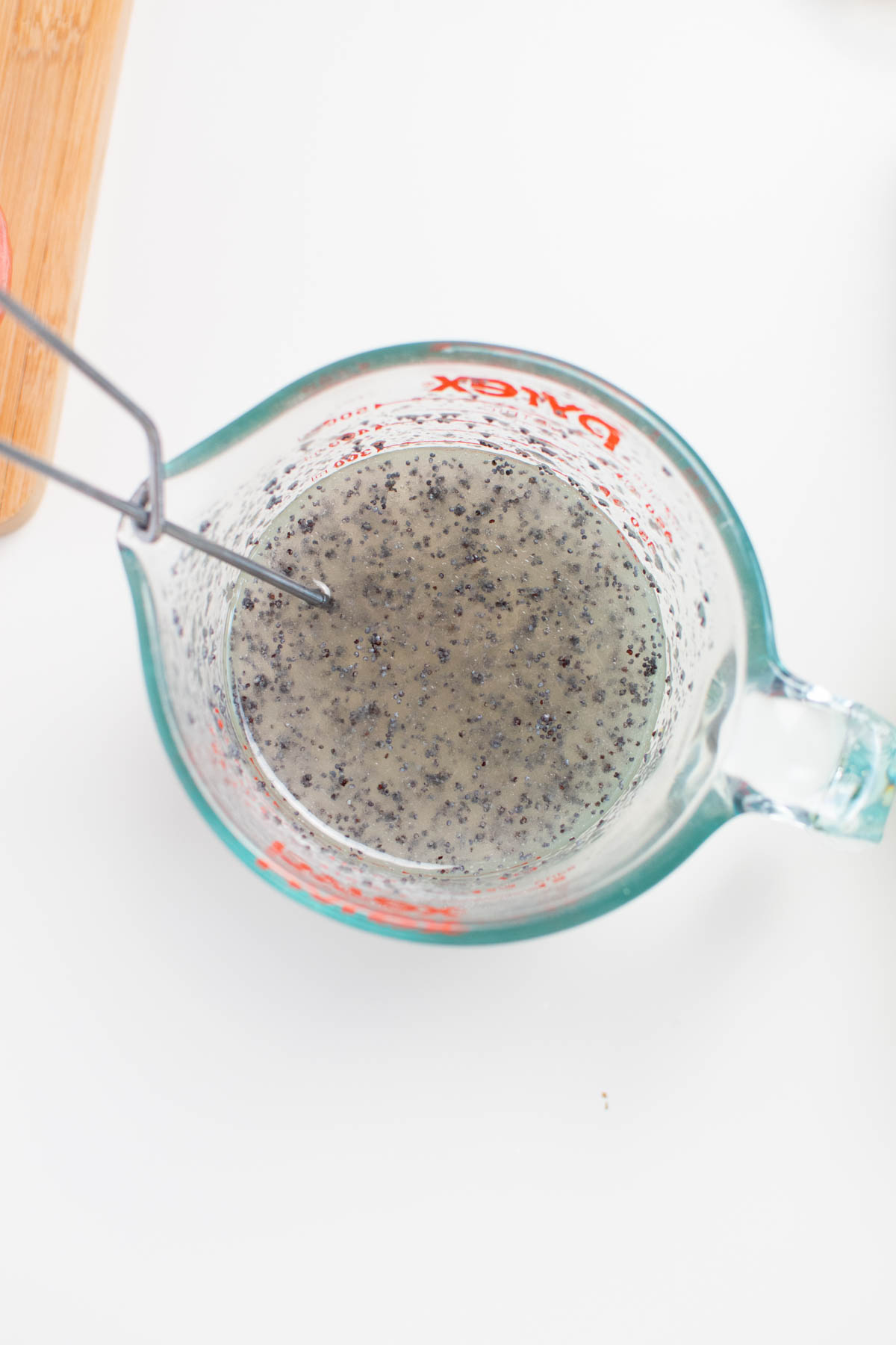 Homemade poppy seed dressing in glass measuring cup with whisk in dressing.