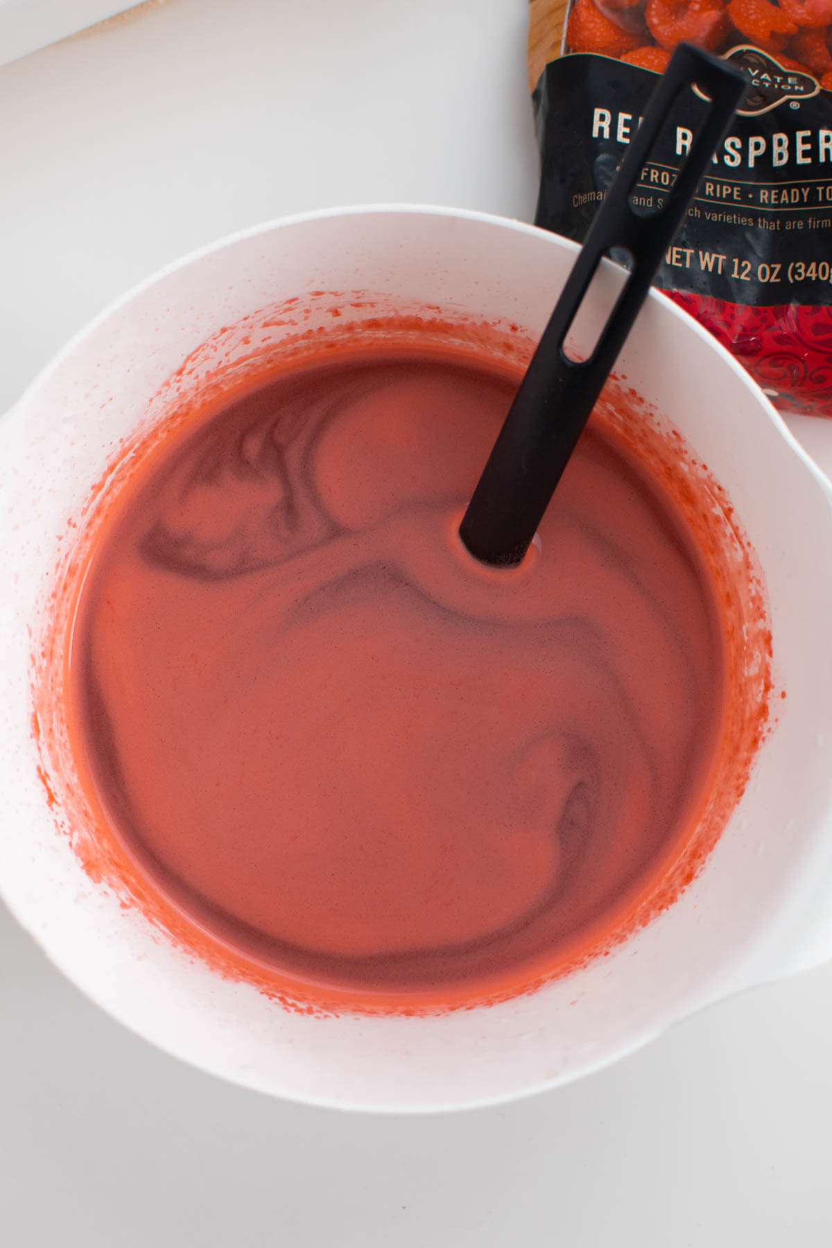 Liquid raspberry Jello in white bowl with black spoon.