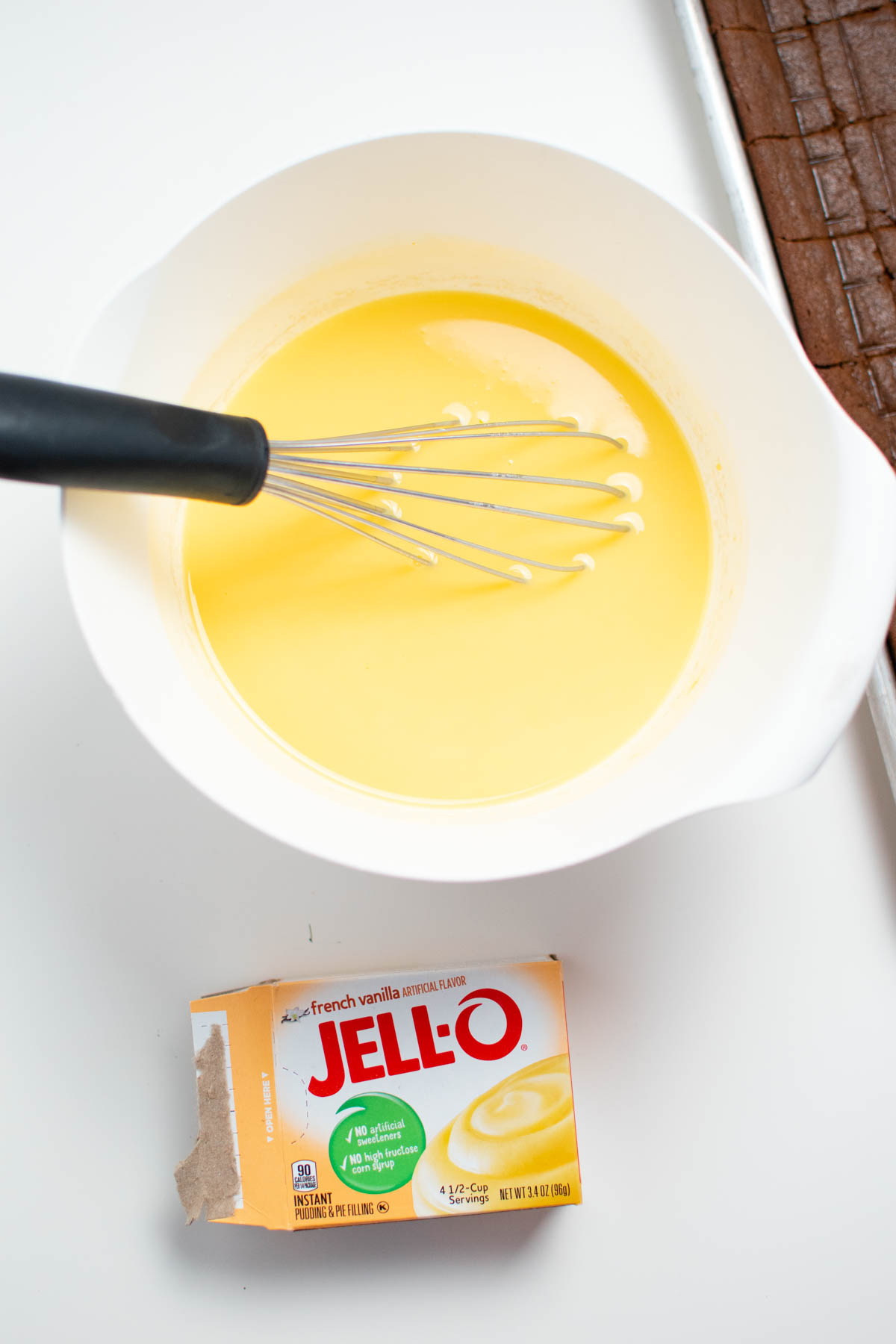 Vanilla pudding in white bowl with whisk and empty Jello pudding box nearby.